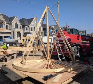 Framing of cone-shaped turret roof structure on job site in front of custom homes